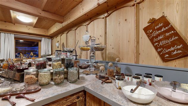 A cozy kitchen with wooden walls that displays a wide selection of storage jars and food. Various ingredients and a note can be seen on the counter.
