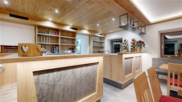 A modern bar with a wooden counter area and warm lighting accents. In the background, there are shelves with glasses and decorations.