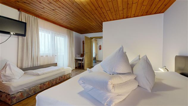 A cozy room with wooden floor and bright wooden ceiling. There is a double bed with many pillows and a single bed on the side.