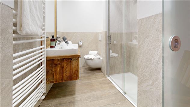 A modern bathroom with a shower and a wooden shelf. The walls are designed with bright tiles and a wood look.