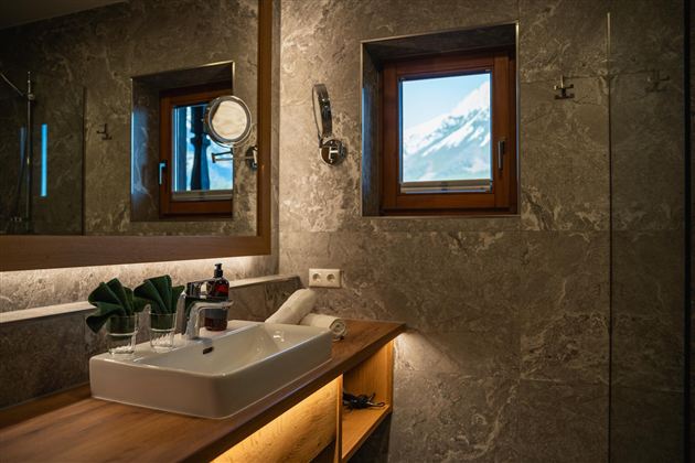 Ein modernes Badezimmer mit einem eleganten Waschbecken und Holzregalen. Durch das Fenster ist eine beeindruckende Berglandschaft zu sehen.