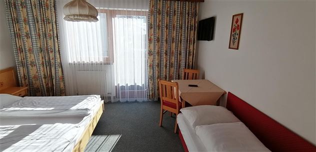 A cozy hotel room with two single beds and a table. Large windows provide plenty of daylight.