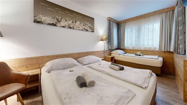 A cozy room with two single beds and an additional bed. The decor is modern with wooden elements and plenty of natural light.