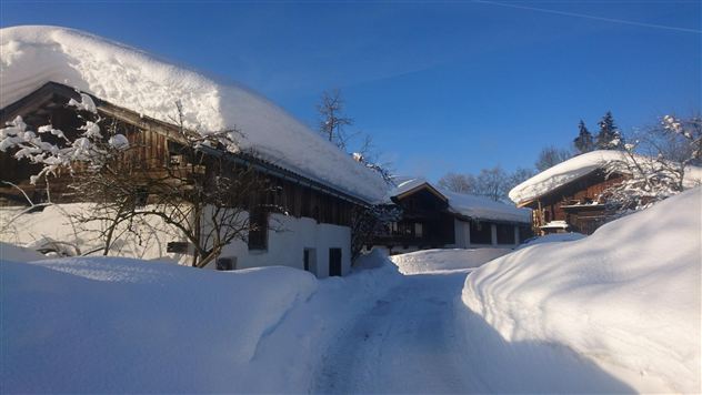 Een besneeuwd landschap met traditionele houten huizen. De lucht is helder en blauw, en de weg is goed zichtbaar.