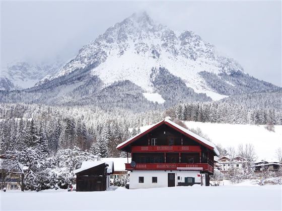 Eine malerische Berglandschaft mit schneebedeckten Gipfeln und einem traditionellen Chalet im Vordergrund. Der Winterzauber schafft eine ruhige und idyllische Atmosphäre.