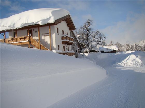 Ein verschneites Haus steht in einer winterlichen Landschaft. Der Schnee ist hoch und bedeckt die Umgebung.