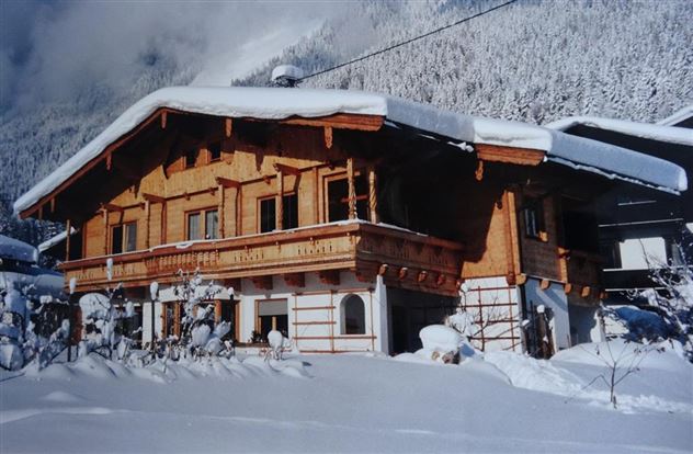 Ein charmantes Holzhaus im Schnee, umgeben von winterlicher Landschaft. Die Fassade ist traditionell gestaltet und die Umgebung ist friedlich und schneebedeckt.