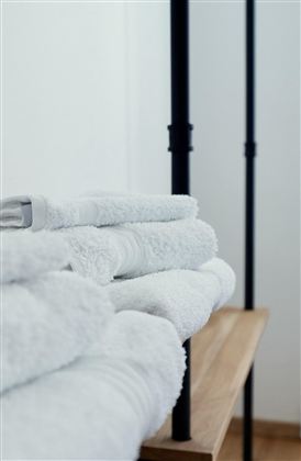 Gestapelte, saubere, weiße Handtücher auf einem Holzregal. Im Hintergrund sind stilvolle Stangen sichtbar.