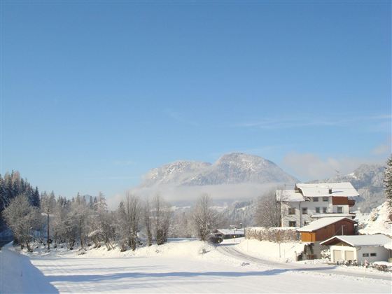 Eine verschneite Landschaft mit Bergen im Hintergrund. Ruhige Häuser und Bäume sind ebenfalls zu sehen.
