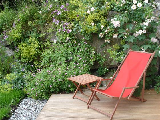 A comfortable red deck chair stands on a terrace. Surrounded by green plants and colorful flowers, the place offers a relaxed atmosphere.