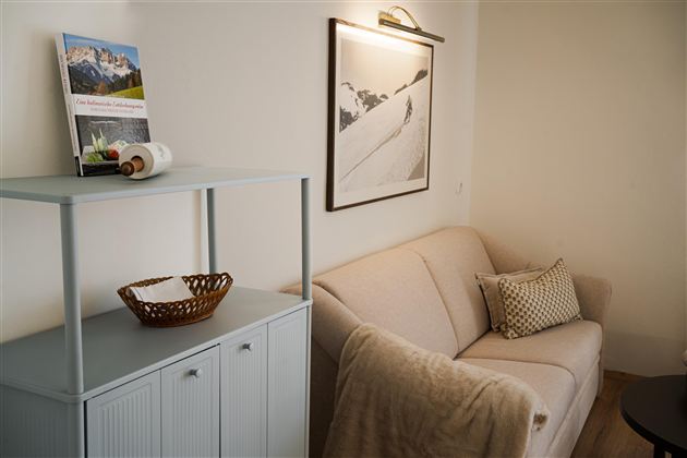 Een gezellige woonkamer met een beige bank en een kleine tafel. Aan de muur hangt een zwart-wit foto van een berglandschap.