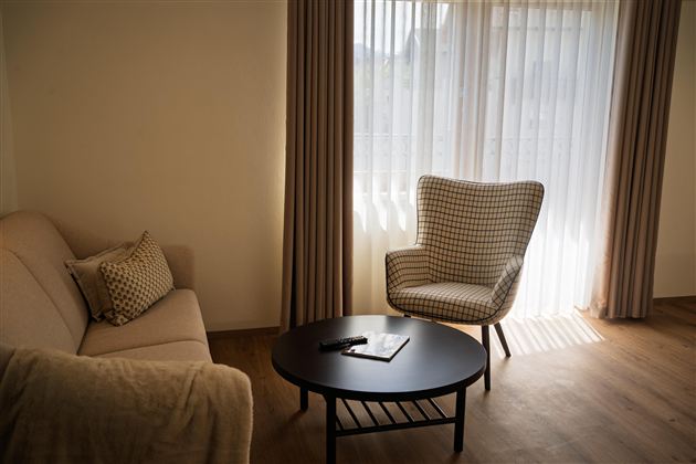 Een gezellige woonkamer met een lichte bank en een comfortabele fauteuil. Het licht stroomt door de gordijnen en creëert een uitnodigende sfeer.