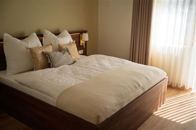 Een moderne slaapkamer met een groot bed en gezellige kussens. Licht stroomt door het venster en creëert een warme sfeer.