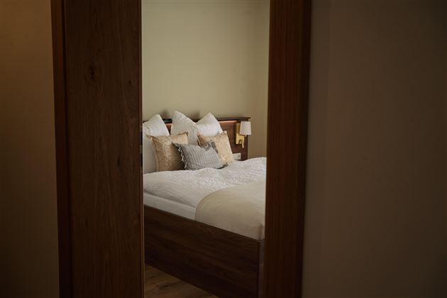Een gezellige slaapkamer met een groot bed en veel kussens. De muren zijn in zachte kleuren gehouden en er is natuurlijk licht.