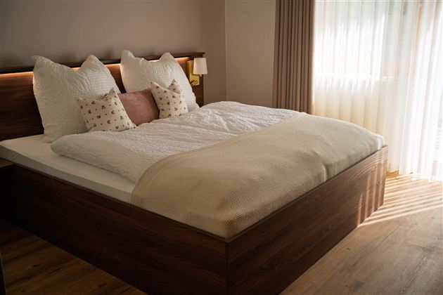 Een moderne slaapkamer met een groot bed en fluffy kussens. Zacht licht valt door de ramen en zorgt voor een gezellige sfeer.