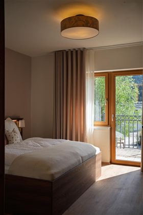 Een gezellige slaapkamer met een tweepersoonsbed. De kamer heeft grote ramen die veel licht binnenlaten en uitzicht op het balkon bieden.