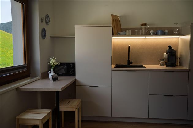 Een moderne keuken met minimalistische meubels en een kleine tafel. Het licht verlicht het aanrecht en creëert een uitnodigende sfeer.