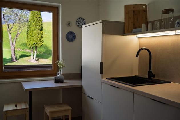Een moderne keuken met een heldere werkblad en een zwarte gootsteen. Door het raam zijn groene bomen en een zonnig landschap te zien.