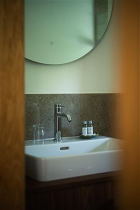 Een elegant badkamer met een wit wastafel en een moderne kraan. Een ronde spiegel en een glas water completeren de stijlvolle ambiance.
