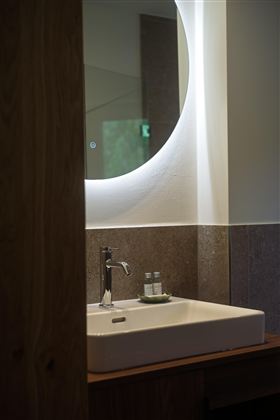 Een modern badkamer met een elegant wastafel en een ronde spiegel. Op de plank staan twee flesjes.