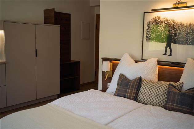 Een moderne slaapkamer met een tweepersoonsbed en stijlvolle kussens. Op de achtergrond bevindt zich een kast en een kunstwerk met een winterlandschap.