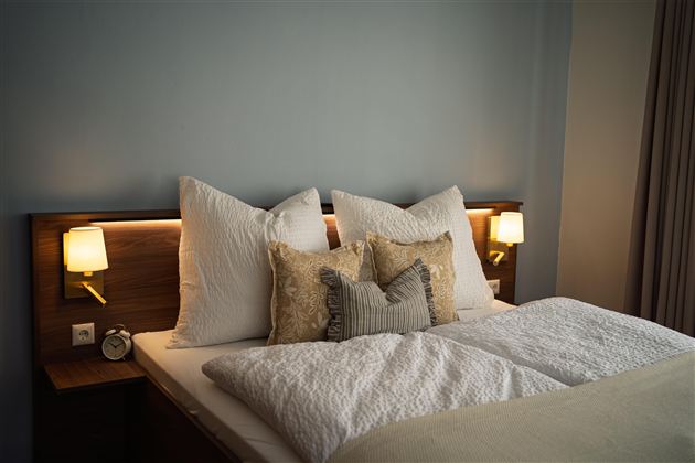 Een gezellige slaapkamer met een groot bed. De kamer is in zachte kleuren ingericht en heeft twee nachtlampjes aan de zijkanten.