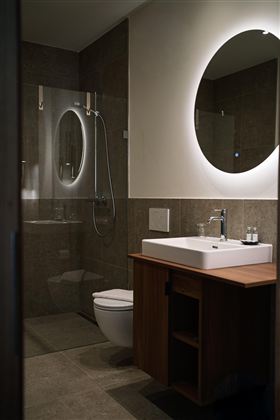 Een moderne badkamer met een douche, een wastafel en een grote spiegel. De warme kleuren en de minimalistische inrichting creëren een uitnodigende sfeer.