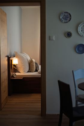 Een gezellige kamer met een bed, dat is uitgerust met grote kussens. Op de achtergrond staat een lamp en decoratieve borden aan de muur.