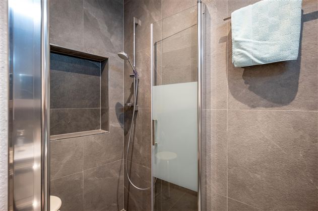 Eine moderne Dusche mit grauen Fliesen und einer klaren Glasabtrennung. Ein Handtuch hängt an einem Halter, während ein Duschkopf sichtbar ist.