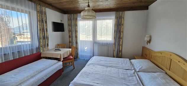 Een gezellig slaapkamer met twee bedden en een extra slaapbank. Grote ramen bieden veel licht en uitzicht naar buiten.