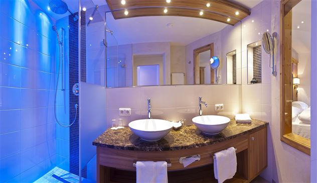 A modern bathroom with two sinks and an elegant shower. Bluish light creates a relaxed atmosphere.