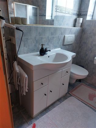 Ein einfaches Badezimmer mit einem weißen Waschbecken und einem WC. Die Wände sind gefliest und es gibt Handtücher sowie einen Teppich auf dem Boden.