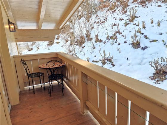 A small balcony with a table and two chairs. In the background, there is snow and a grassy area.