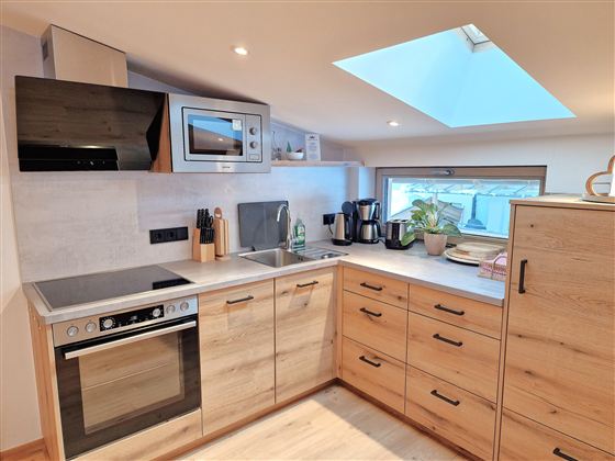 A modern kitchen with wooden cabinets and appliances. A window with a skylight provides plenty of light.