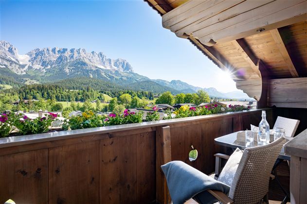 Ein schöner Balkon mit Blick auf die Berge und eine grüne Landschaft. Sonnenschein und Blumen verleihen der Szene eine einladende Atmosphäre.