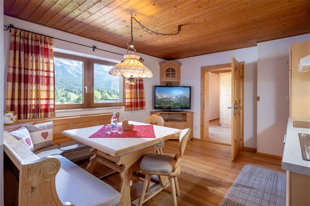 Eine gemütliche Küche mit einem Holztisch und Stühlen. Die Fenster bieten einen Blick auf die Berge, und es gibt einen Fernseher in der Ecke.