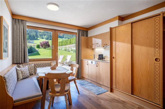 Eine gemütliche Ferienwohnung mit Holzinterieur und schöner Aussicht auf die grüne Landschaft. Der Raum bietet eine kleine Küche und einen Essbereich mit Tisch und Stühlen.