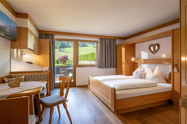 Ein gemütliches Zimmer mit einem Doppelbett und Holzmöbeln. Durch das Fenster schaut man auf eine grüne Landschaft.