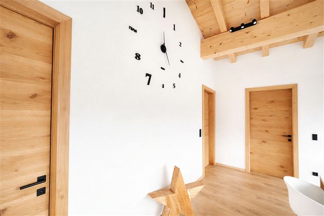 A bright room with wooden details and a large clock on the wall. There are two doors and a decorative wooden star figure on the floor.