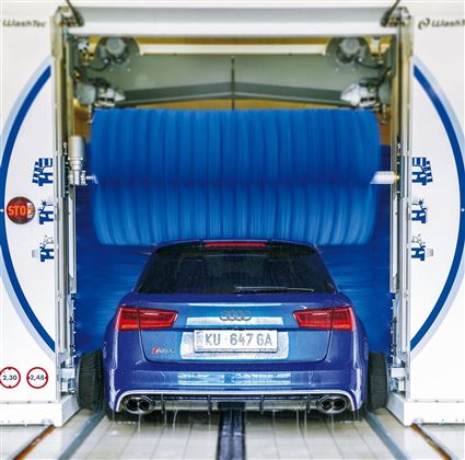 Een blauwe auto in een carwash met grote blauwe borstels. De carwash is open en de auto wordt schoongemaakt.