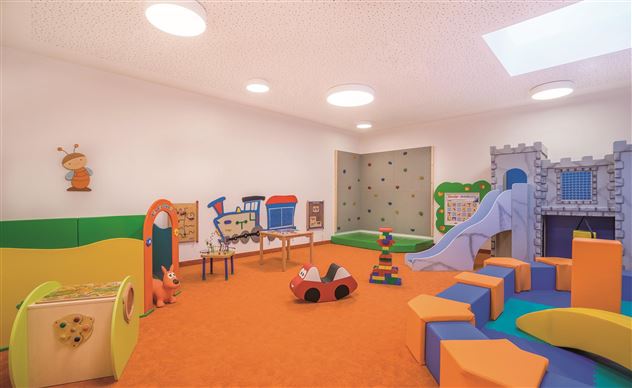 Een kleurrijke speelkamer met verschillende speelgoed en een glijbaan. De muren zijn in heldere kleuren geschilderd en de vloer is oranje.