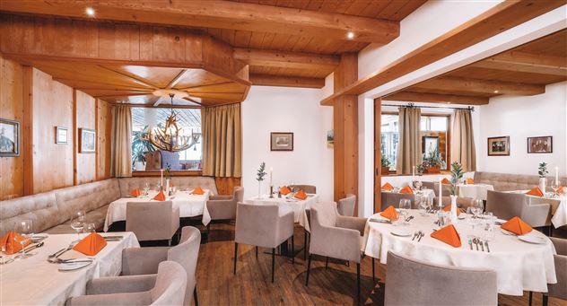 Een elegant restaurant met houten muren en een gezellige sfeer. De tafels zijn gedekt met witte tafelkleden en oranje servetten.