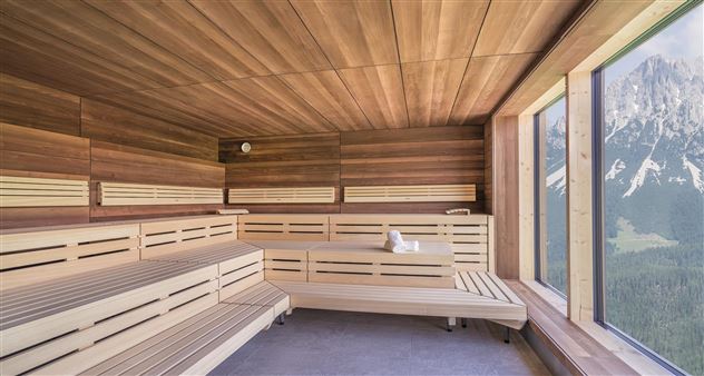 Een moderne sauna van licht hout met grote ramen. Het uitzicht toont een indrukwekkend berglandschap op de achtergrond.