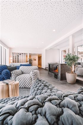 Een modern woonomgeving met gezellige, gevlochten stoelen en een open haard. Grote ramen zorgen voor veel licht en een uitnodigende sfeer.