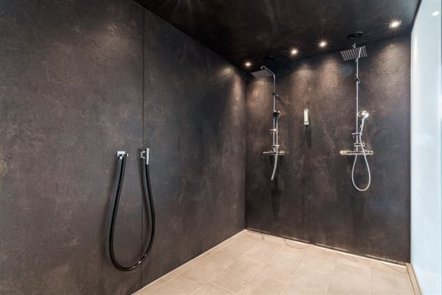 A modern shower with black wall paint and two showerheads. The floor is made of light tiles.