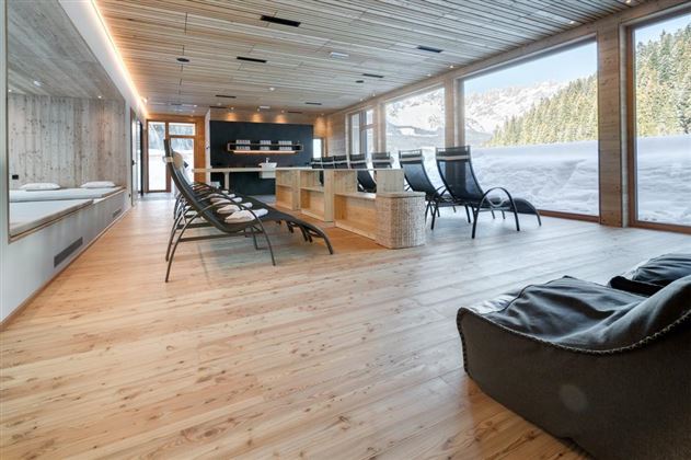 A modern wellness area with wooden floors and large windows that offer a view of snow-covered mountains. There are comfortable loungers and an open reception area.