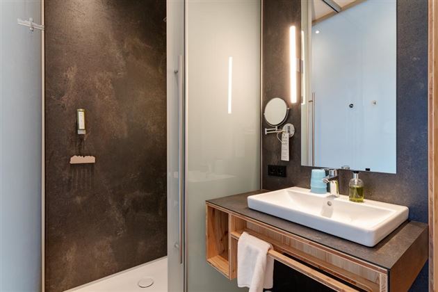 A modern bathroom with a shower and an elegant sink arrangement. The walls are in dark shades, complemented by bright lighting.