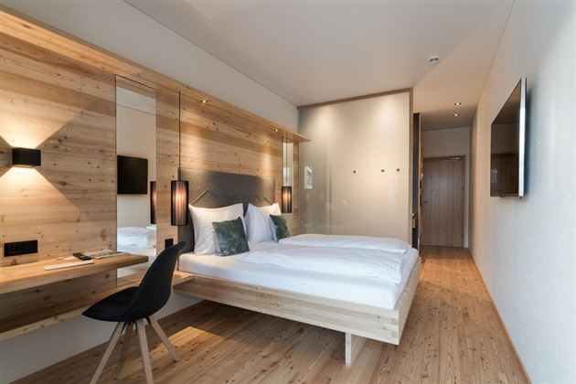 A modern bedroom with a wooden bed and elegant furnishings. Large windows provide plenty of light and a cozy atmosphere.