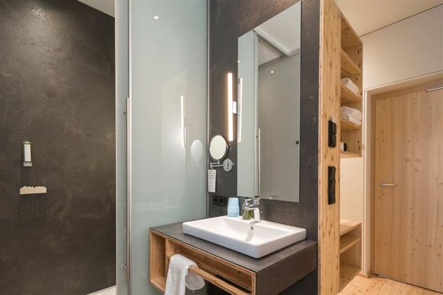 A modern bathroom with a glass shower and a stylish sink unit. The walls are done in dark and warm wood tones.