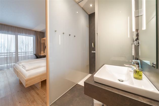 A modern hotel room with a clean and minimalist design. On the left, you can see a comfortable bed, and on the right, a bathroom with an elegant sink.
